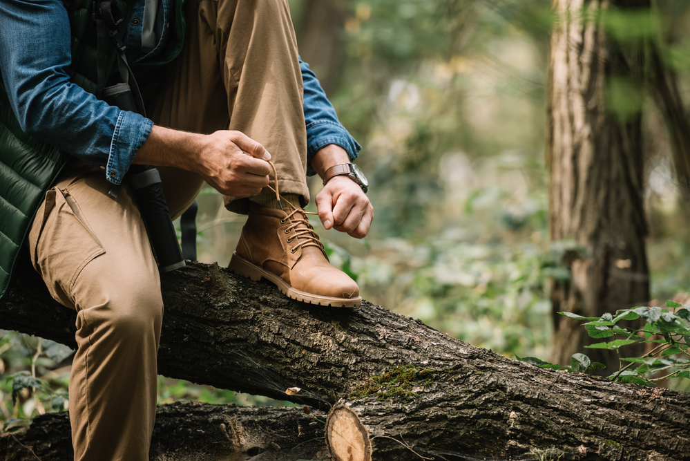 A man sitting on a fallen tree trunk lacing his boots. | Hiking near Bentonville, AR.