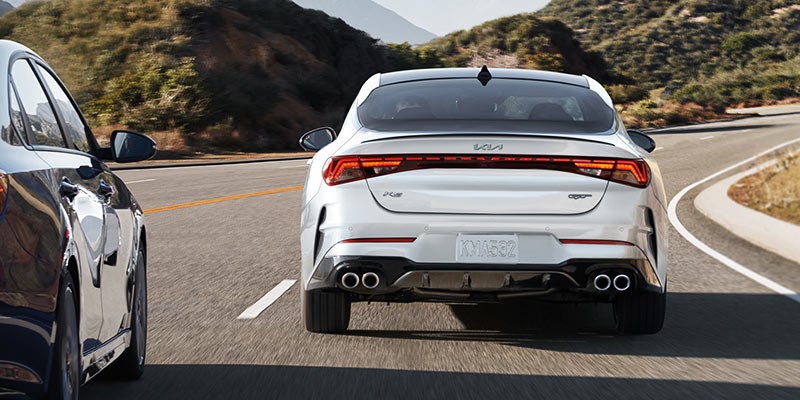 Rearview of a white 2022 Kia K5 being driven on the highway. | Kia dealer in Bentonville, AR.