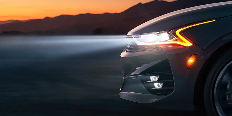 Front view of a white 2022 Kia K5 with the headlights on. | Kia dealer in Bentonville, AR.