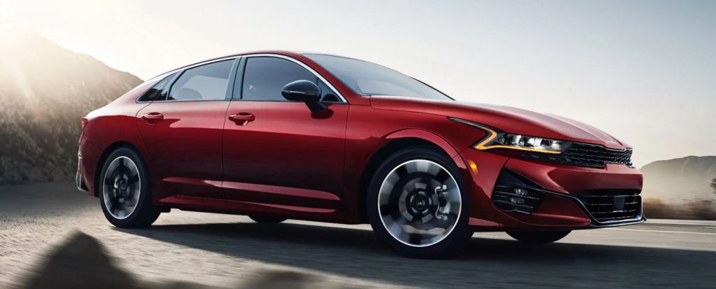 Profile view of a red 2022 Kia K5 being driven on the road. | Kia dealer in Bentonville, AR.