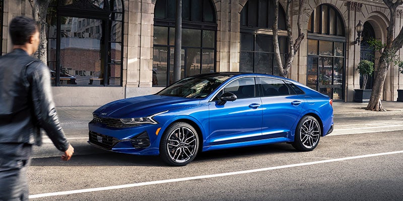 A royal blue 2022 Kia K5 parked on the road in front of a building. | Kia dealer in Bentonville, AR.