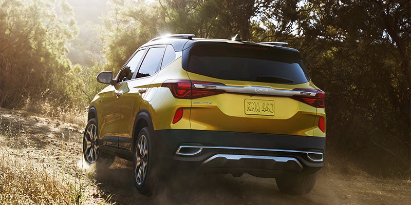 Rearview of a golden yellow 2022 Kia Seltos parked in a wooded area. | Kia dealer in Bentonville, AR.