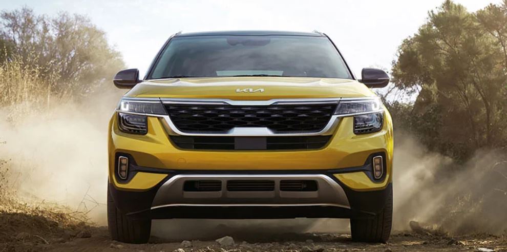 Front view of a golden yellow 2022 Kia Seltos parked on a dirt road with trees in the background. | Kia dealer in Bentonville, AR.
