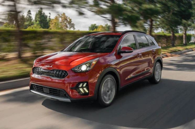 A red 2022 Kia Niro being driven on the road with trees in the background. | Kia service center in Bentonville, AR.