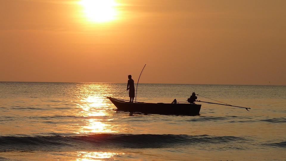 A man on his boat fishing with the sun setting in the background. | Boating destinations in Bentonville, AR.
