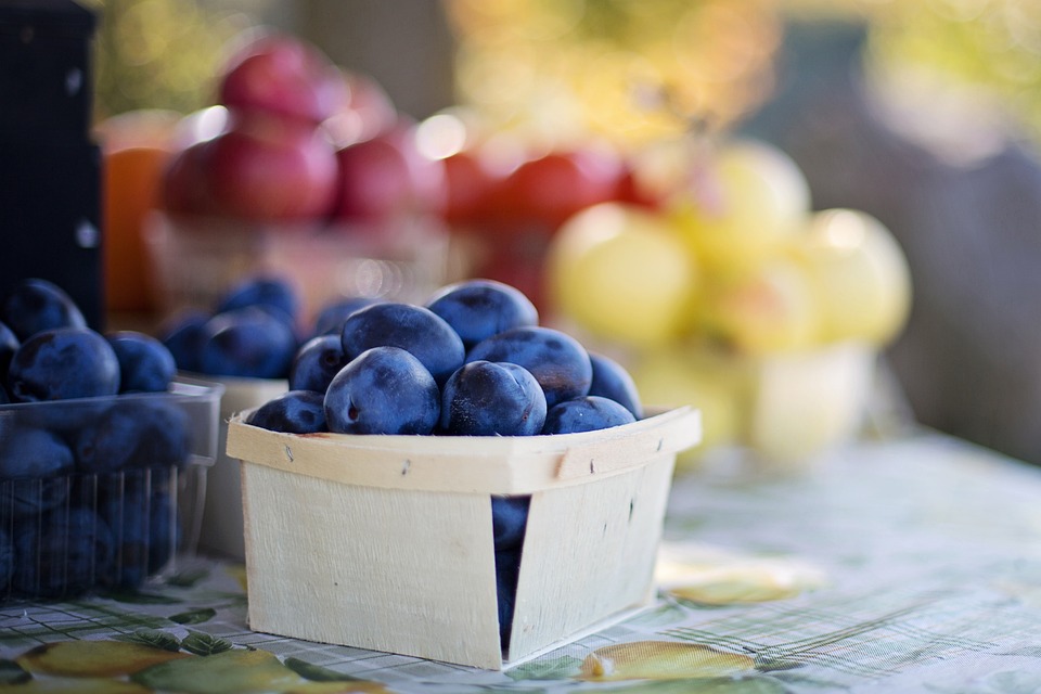 A small basket of plums with other fruits in the background. | Farmers' markets around Bentonville, AR.