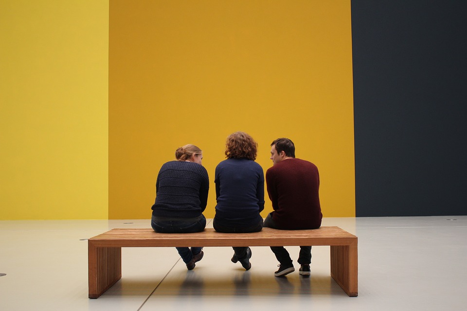 Three people sitting on a bench in front of a yellow wall inside of a museum. | Tourist attractions around Bentonville, AR.