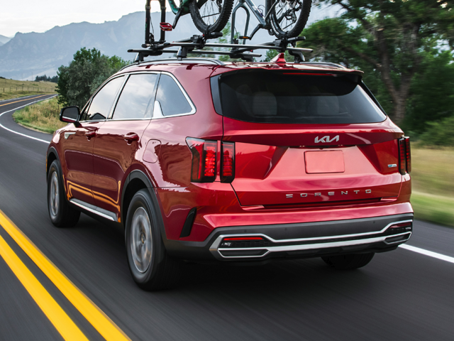 A red 2023 Kia Sorento Hybrid being driven on the road with two bikes attached to the roof. | Kia dealer in Bentonville, AR.